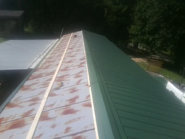 Old rusted panels beside newly installed green metal roofing — Wind Damage Roof Repair by Roofing Brothers in New Ulm
