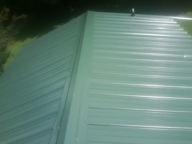 New green metal panels meeting at the ridge of a roof — Flat Roof Repair work by our crew in New Ulm