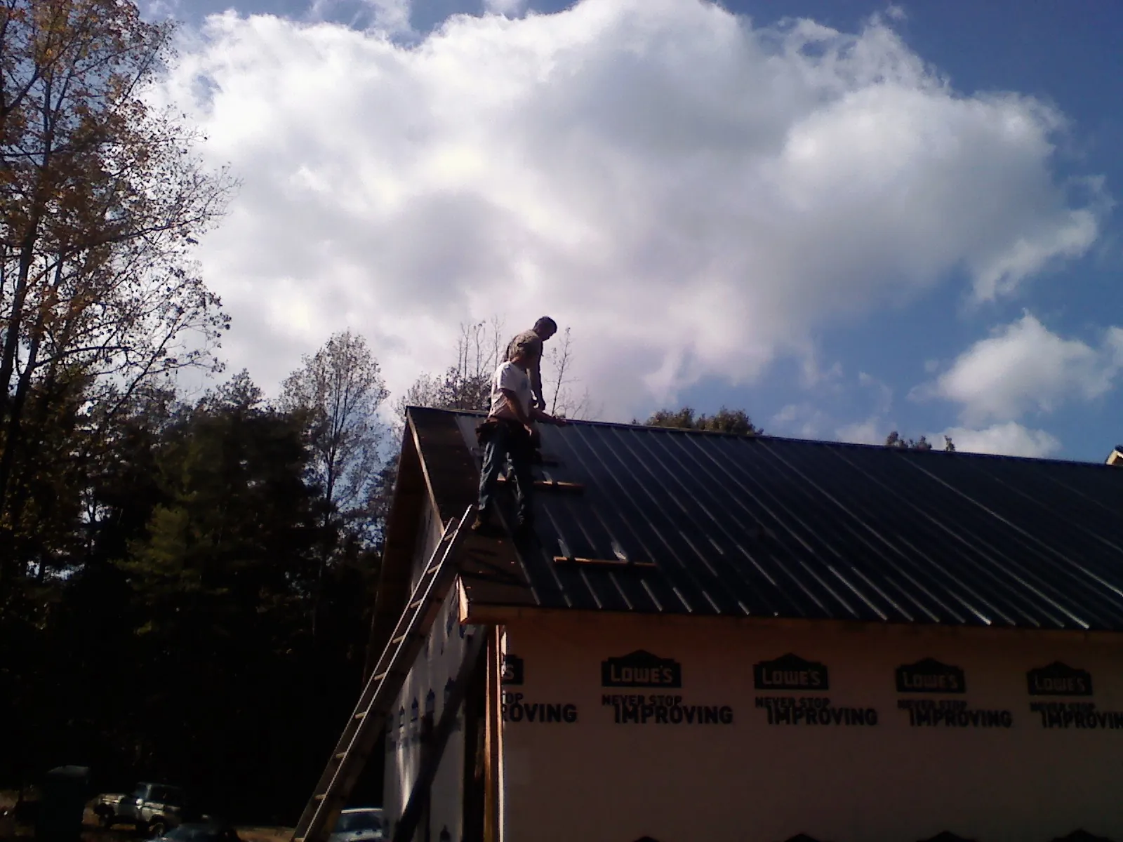 Roofer fastening dark metal panels high against a cloudy sky, from a Roof Inspection job in New Ulm
