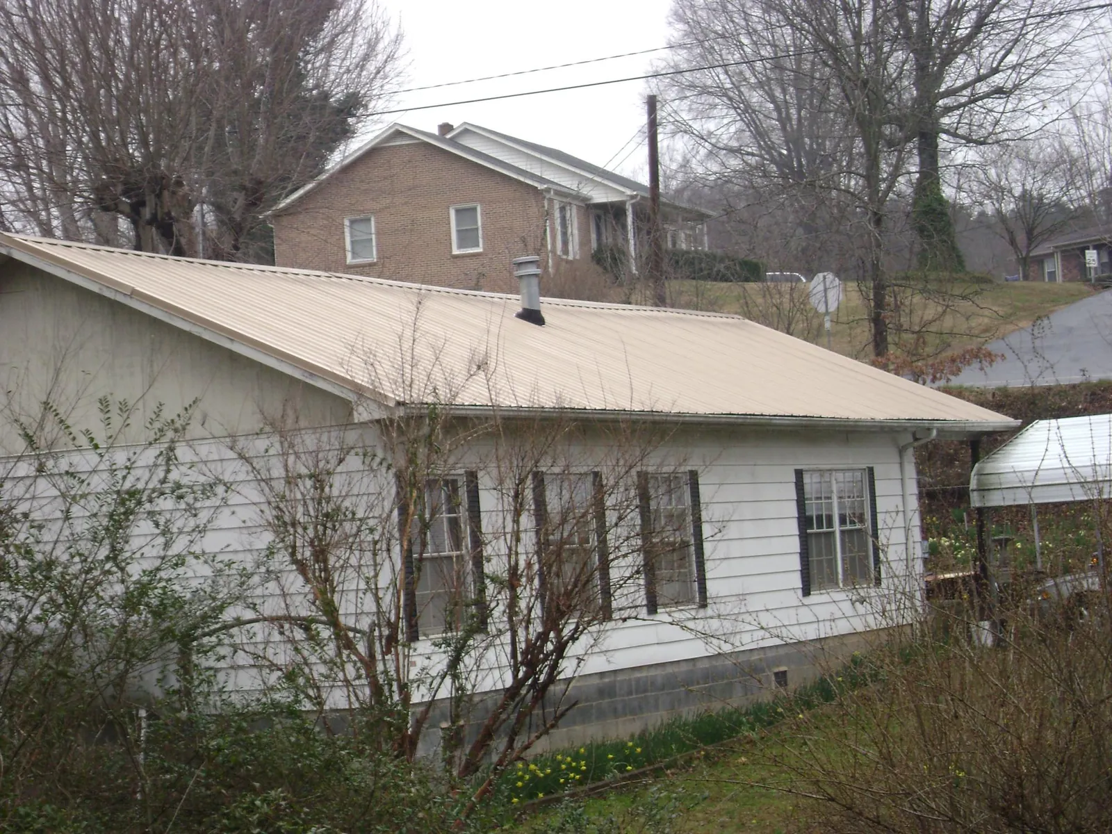 Tan metal roof on a white sided house set into a hillside — Commercial Roofing by Roofing Brothers in New Ulm